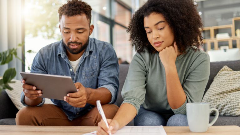 A man and a woman look at a tablet and review documents while sitting on a couch
