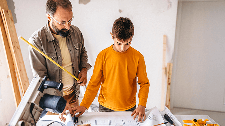 A father and son stand in a construction area reviewing building plans